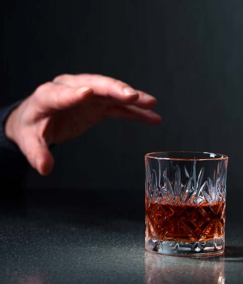 мужчина тянет руку к стакану с алкоголем