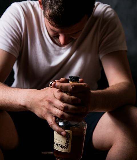 мужчина сидит с бутылкой алкоголя, опустив голову